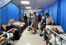 Humanitarian Crisis Deepens as Gaza Hospitals Ordered to Evacuate Patients and family members crowd a hospital corridor in Gaza, with beds lined along both sides and blue curtains dividing sections.